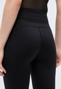 Κοντινό πλάνο ενός ατόμου που φοράει μαύρο κολάν με ψηλή μέση και ορατές ραφές κατά μήκος της ζώνης μέσης και της πλάτης.