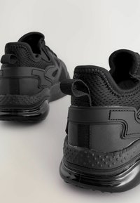 Svarta atletiska sneakers som har en kombination av strukturerad mesh och släta syntetiska material, med en vadderad sula och förstärkt häl.