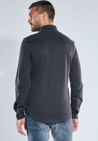 Dunkelgraues Langarmhemd mit Kragen, mit Knopfmanschetten und einer glatten Textur. Getragen mit blauen Jeans, die eine legere Passform zeigen.