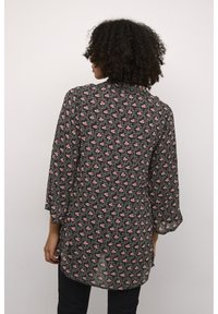 Blouse noire à fleurs avec des manches trois-quarts ; présente un petit motif de fleurs roses et un ourlet arrière légèrement plus long. Tissu léger.