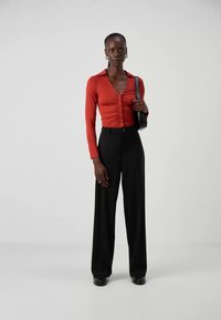 Rotes Langarmhemd mit Knopfleiste und gerafftem Design, kombiniert mit hoch taillierten schwarzen weit geschnittenen Hosen. Schwarze Handtasche, schicke Schuhe.