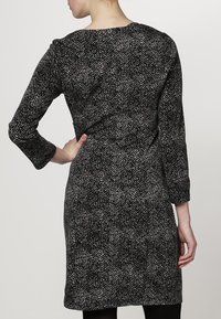 Robe texturée noir et blanc à manches longues, avec un col rond et une silhouette ajustée, affichant un motif subtil sur l'ensemble.