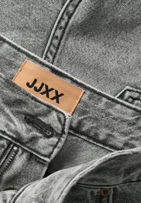 Giacca in denim grigio con finitura testurizzata, dettagli cuciti e etichetta in pelle con "JJXX" in lettere nere.