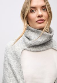 Sciarpa grigia in misto lana con una texture morbida e un design con colletto alto, caratterizzata da un dettaglio spalle scoperte, indossata sopra un top chiaro.