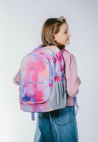 Mnohobarevný batoh s květinovým akvarelovým vzorem v odstínech růžové, fialové a oranžové. Hladká textura, nastavitelné ramenní popruhy a zipové kapsy.