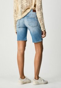 Shorts de mezclilla en azul claro, con una sutil textura desgastada. Presentan un diseño de cinco bolsillos y un dobladillo vuelto. Combinados con zapatillas blancas.
