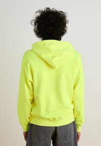 Neon yellow hooded sweatshirt with a relaxed fit and ribbed cuffs, featuring a kangaroo pocket and soft texture. Back view shown.