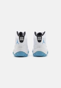 Balti sportiniai bateliai su lygiu oda, juodais akcentais ant kulno, mėlynu padu ir žinomu Jumpman logotipu mėlyna spalva ant nugaros.