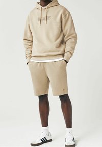 Sudadera beige con la impresión "Los Ángeles", pantalones cortos beige a juego y calcetines blancos. Footwear presenta rayas negras sobre un diseño blanco. Tejido suave.