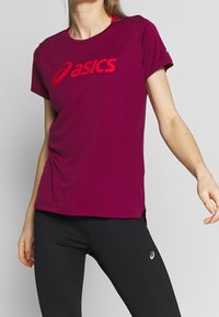 Camiseta deportiva burdeos en tejido ligero con un gran logotipo rojo de "asics". Manga corta y escote redondo con aberturas laterales.
