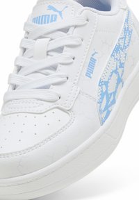 Fehér sneaker, textúrált felülettel, kék kiegészítőkkel és perforált lábujjrésszel. Lapított fűzőkkel és mintázott oldalsó panelekkel rendelkezik, amelyeken feltüntették a márkát.
