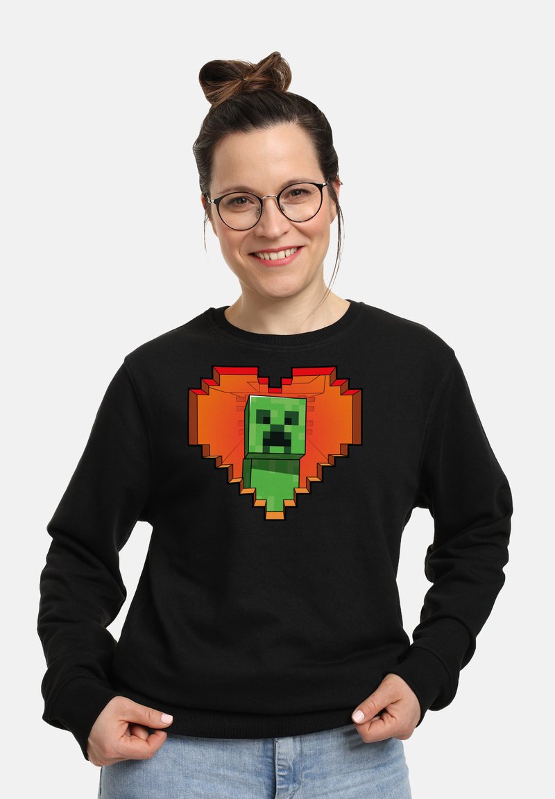 Felpa nera con un personaggio verde pixelato al centro di un design a forma di cuore con accenti arancioni. Materiale in cotone, vestibilità casual.