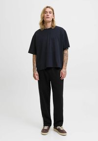 Sort kortærmet t-shirt med afslappet pasform, parret med sorte bukser og brune sko, som viser et afslappet, komfortabelt look.
