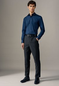 Camicia azzurra a maniche lunghe, pantaloni eleganti neri e scarpe nere. La camicia presenta un colletto appuntito e chiusura con bottoni.