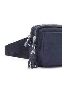 Navy blue nylon crossbody bag with two zippered compartments, textured surface, and a rubber monkey keychain attached to the zipper pull.