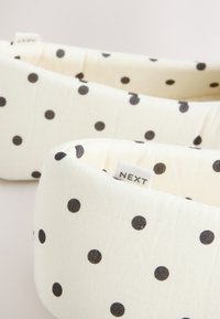 Deux bandeaux en tissu couleur crème à pois noirs, l'un net montrant une petite étiquette "NEXT" cousue à l'intérieur.