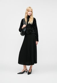 Melna sequined īsā jaka, melna plīšu midi svārki, melnas siksniņas papēžu kurpes un melna plecu soma. Vientuļas krāsas, spīdīgas tekstūras.