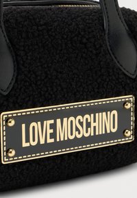 Borsa nera con superficie in tessuto testurizzato e dettagli in pelle. Presenta un'etichetta rettangolare in oro con la scritta "LOVE MOSCHINO".