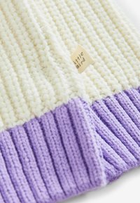 Bonnet tricoté en crème et lavande. Présente un motif texturé, un revers côtelé et une étiquette en tissu portant la mention "little bird".