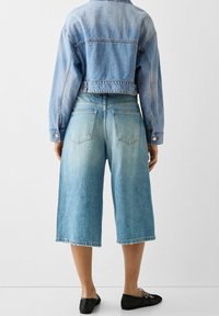 Hellblaue Jeansjacke mit kurzem Schnitt und langen Ärmeln, kombiniert mit passenden weiten Jeans-Culottes mit ausgefranstem Saum.