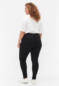 Black leggings with a high waist, featuring a smooth texture, two back pockets, and a fitted design. Paired with a white short-sleeve top.