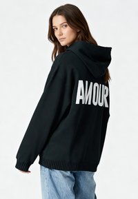 Felpa nera con cappuccio e vestibilità oversize, caratterizzata dalla scritta "AMOUR" in bianco sul retro, polsini e orlo a costine.