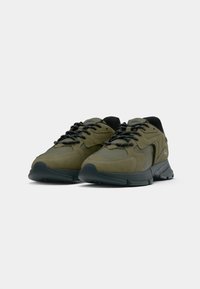 Green athletic shoes featuring a combination of smooth and textured materials, thick black soles, and contrasting black laces.