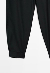 Zwarte broek van een gladde stof, met een taps toelopende pijp en omslag onderaan. Eenvoudig ontwerp, zonder opvallende patronen of bevestigingsmaterialen.