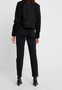 Černá kožená bunda s klasickým límcem, nošená přes černé džíny s vysokým pasem. Oblečení doplňují špičaté kotníkové boty a krátký střih.