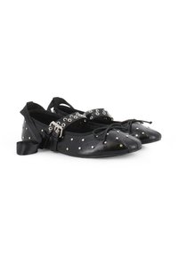 Bailarinas de cuero negro con tachuelas plateadas, una correa con ojetes plateados y un lazo de satén en el tobillo. Punta redondeada y tacón bajo.