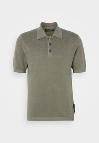 Polo en maille vert olive à manches courtes avec trois boutons et finitions côtelées, avec un col plié et une petite étiquette de marque latérale.