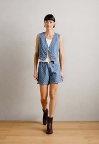 Zils rakstots veste ar pogām, kopā ar atbilstošām šortiem. Modelis valkā baltu topu un brūnas potīšu zābaciņus. Vienkāršs dizains, ikdienišķs piegriezums.