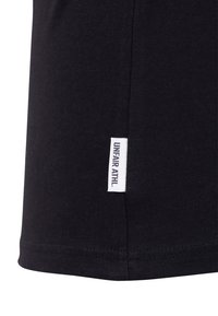 Melnas kokvilnas T-krekls ar noapaļotu apakšmalu, kuram sānos ir balta auduma birka ar melnu tekstu "UNFAIR ATHL."