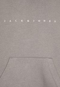 Siva kapuca z središnjim kenguru žepom, rebrastim manžetama i rubom, s natpisom "JACK & JONES" otisnutim bijelom bojom na prsima.