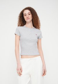 Γκρι εφαρμοστό κοντομάνικο μπλουζάκι από απαλό ύφασμα, με στρογγυλή λαιμόκοψη, πέντε κουμπιά στη λοξή κλειστή πατιλέτα και μικρό ροζ λογότυπο στο στήθος.