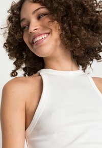 Top de tanque branco com nervuras, com um decote alto e alças largas, apresentando um design justo que acentua os contornos do corpo.