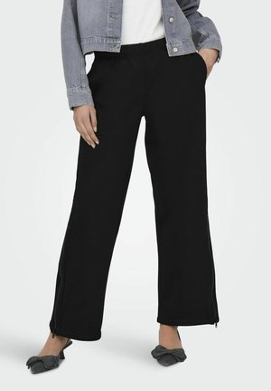 Pantaloni negri cu picior larg, confecționați dintr-un material moale, având accente cu fermoar pe laterale la tivuri și o talie elastică pentru confort. Asortați cu o jachetă din denim.