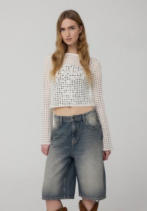 Maglietta bianca a maniche lunghe cropped con motivo a trama aperta, abbinata a pantaloni corti in denim blu sbiadito, caratterizzati da una vestibilità comoda e tasche grandi.