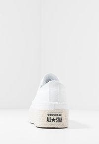 Sneaker bianca in tela con una robusta suola in stile espadrillas, caratterizzata da un'etichetta nera "CONVERSE ALL STAR" sul tallone e un bordo texturizzato.