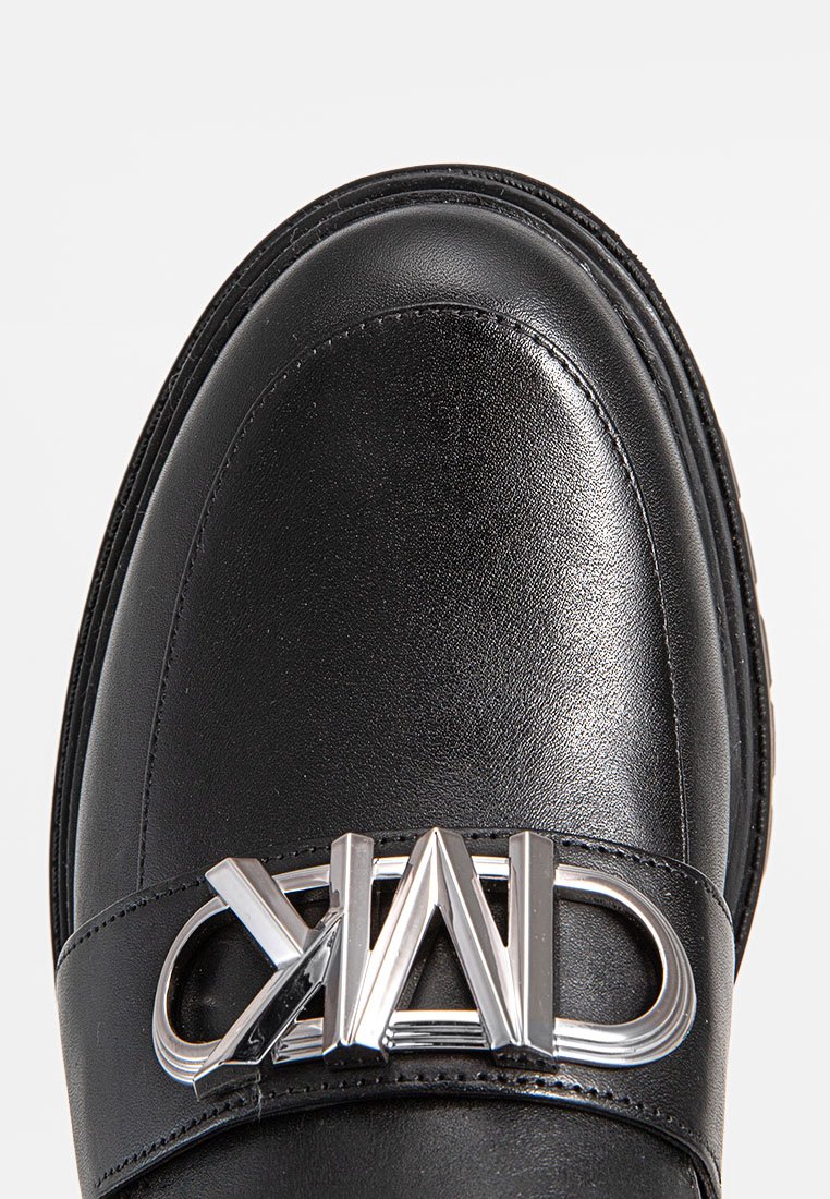 Scarpa di pelle nera con punta arrotondata, caratterizzata da una cinturino con logo argentato lucido e dettagli in cucitura lungo i bordi. Texture liscia.