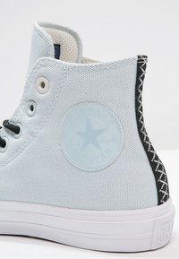 Wysokie trampki w jasnoniebieskim kanwie, z okrągłą łatą z logo, czarnymi teksturowanymi akcentami oraz kontrastującą białą gumową podeszwą.