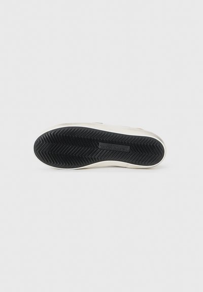 White sneaker sole with a textured black rubber outsole, featuring a herringbone pattern and embossed brand name. Clean, minimal design.