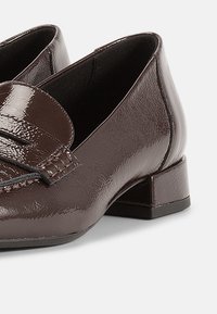 Καφέ λουστρίνι μοκασίνια με χαμηλό τακούνι μπλοκ, με διακοσμητικό λουράκι στο πάνω μέρος και λεία, γυαλιστερή υφή.