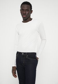 Camisa branca de mangas longas combinada com jeans azul escuro. A camisa tem um decote redondo e é feita de um tecido suave. Os jeans possuem um design clássico de cinco bolsos.