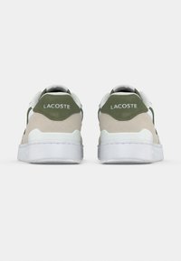 Ζευγάρι λευκών και μπεζ αθλητικών παπουτσιών Lacoste με πράσινες λεπτομέρειες, εμφανιζόμενα από πίσω σε απλό λευκό φόντο.