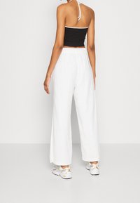 Černý crop top s bílým lemováním, spárovaný s volně střiženými bílými kalhotami. Bílé tenisky dokončují celý outfit. Hladká, lehká tkanina.