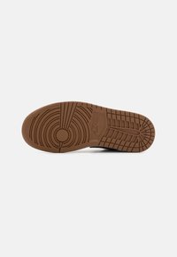 Semelle de basket Nike en caoutchouc marron, présentant des motifs de bande de roulement circulaires et linéaires, avec un logo embossé et une surface de grip texturée.
