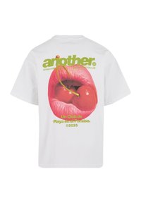 White cotton t-shirt featuring a graphic of pink lips with cherries, green text reading "another" and "Un Club de Playa en el Paraíso."