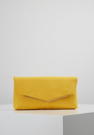 Żółta zamszowa kopertówka z klapką w kształcie litery V i delikatnym przeszyciem, umieszczona na białej geometrycznej powierzchni na tle w jednolitym kolorze.