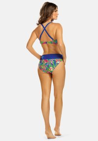 Wielokolorowy zestaw bikini z topem na krzyż, ozdobionym niebieskimi akcentami, oraz wzorowanymi majtkami z tropikalnymi liśćmi w kolorach zielonym, różowym i żółtym.